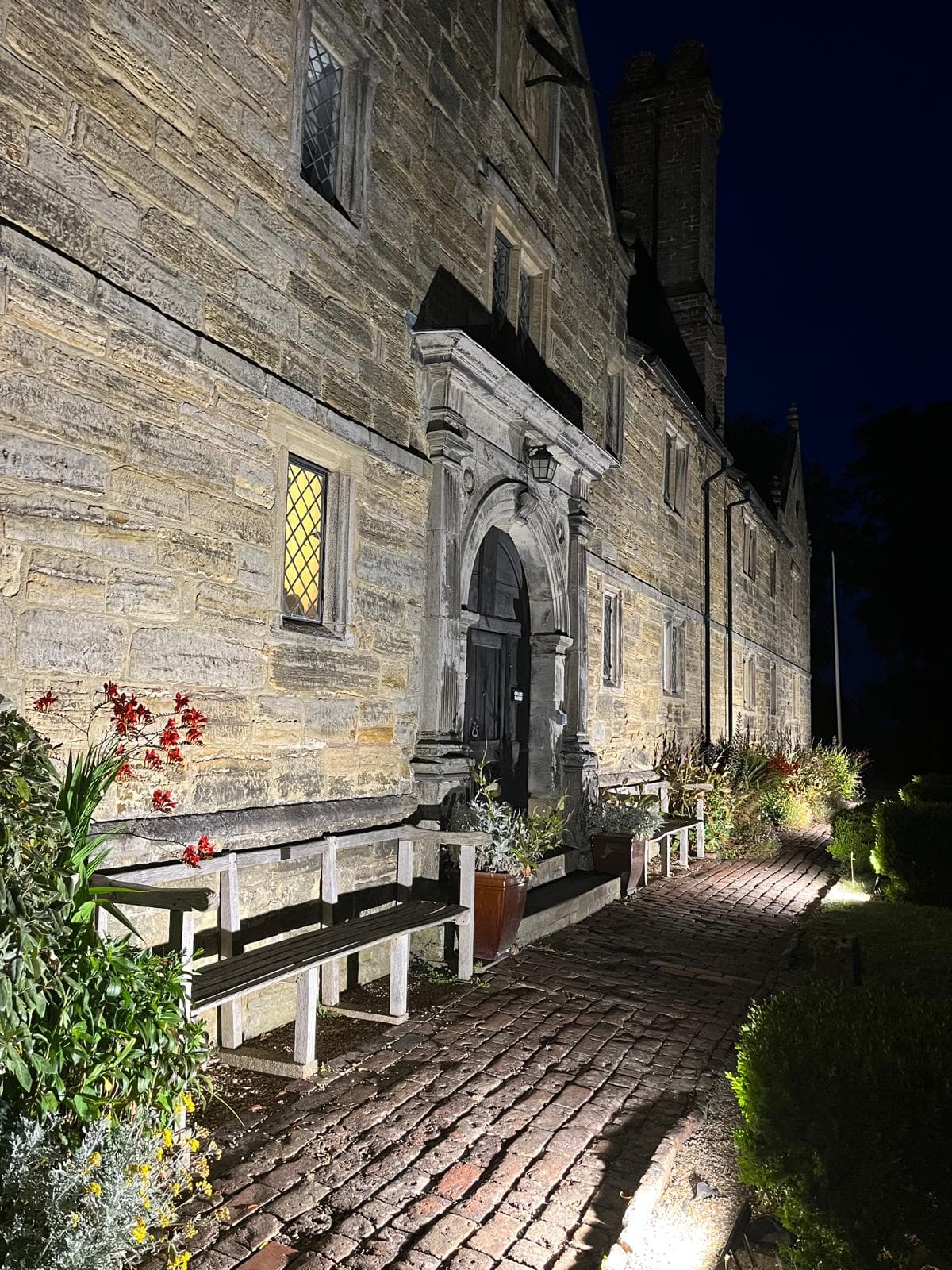 Warm exterior uplighters illuminating the stone entrance of a historic property at dusk.