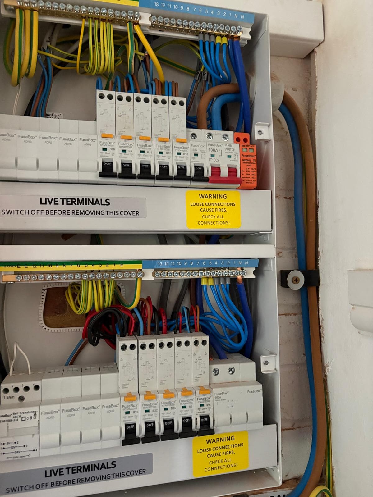 A new metal-clad dual consumer unit with individual RCBO breakers and a surge protection device, mounted in a tidy hallway installation.